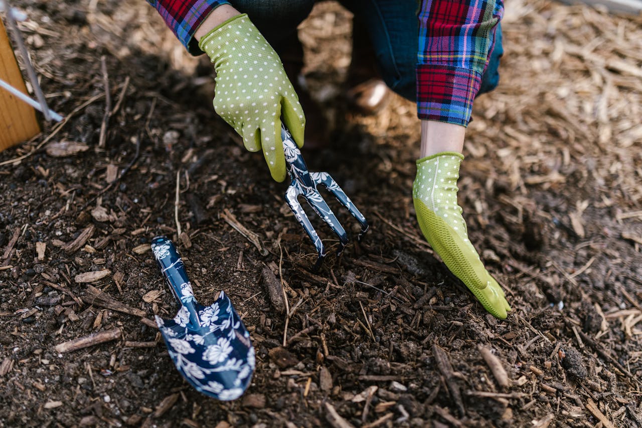 our-services-1 A person wearing gloves using garden tools in soil for planting.